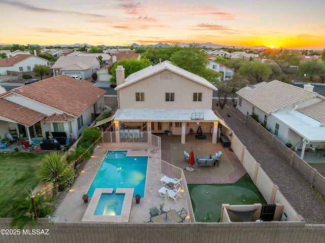 9880 E Cisco Ct, Tucson, AZ 85748 - back of house at dusk with a residential view, a fenced backyard, a pool with connected hot tub, a patio area, and stucco siding