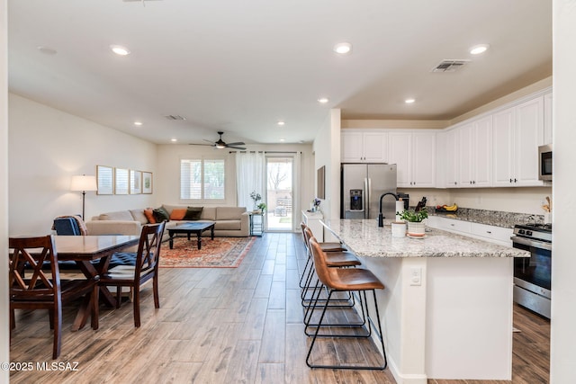 3287 W Sunlit Peak Dr, Tucson, AZ 85742 - kitchen with stainless steel appliances, light wood finished floors, white cabinets, light stone countertops, and open floor plan