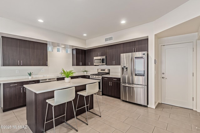 890 E Millenium Ct Unit E, Tucson, AZ 85719 - kitchen with appliances with stainless steel finishes, dark brown cabinets, a kitchen breakfast bar, light countertops, and light tile patterned floors