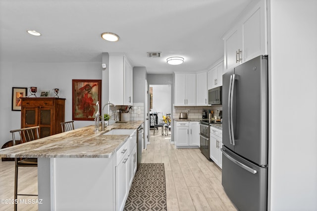 9000 N Twain St, Tucson, AZ 85742 - kitchen with appliances with stainless steel finishes, a peninsula, white cabinets, light wood-style flooring, and tasteful backsplash