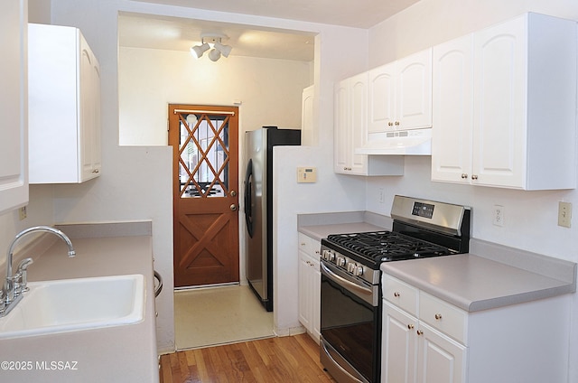 2422 E Drachman St, Tucson, AZ 85719 - kitchen featuring appliances with stainless steel finishes, a sink, under cabinet range hood, light wood-type flooring, and white cabinetry