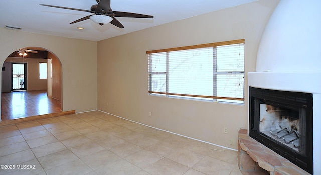 2422 E Drachman St, Tucson, AZ 85719 - unfurnished living room with ceiling fan, arched walkways, a multi sided fireplace, light tile patterned flooring, and baseboards