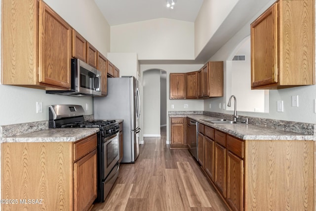 9102 N Safflower Ln, Tucson, AZ 85743 - kitchen with stainless steel appliances, arched walkways, a sink, light wood-style floors, and brown cabinetry