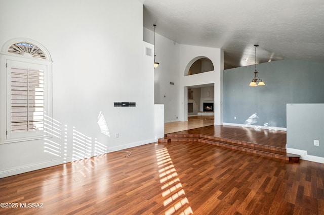 11562 N Scioto Ave, Tucson, AZ 85737 - unfurnished living room featuring wood finished floors, baseboards, high vaulted ceiling, and a lit fireplace