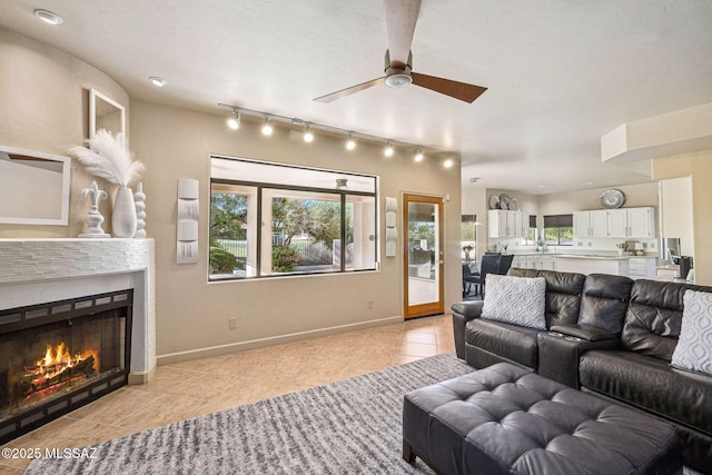 1920 W Canada Hills Dr, Oro Valley, AZ 85737 - living area with light tile patterned floors, rail lighting, ceiling fan, a warm lit fireplace, and baseboards