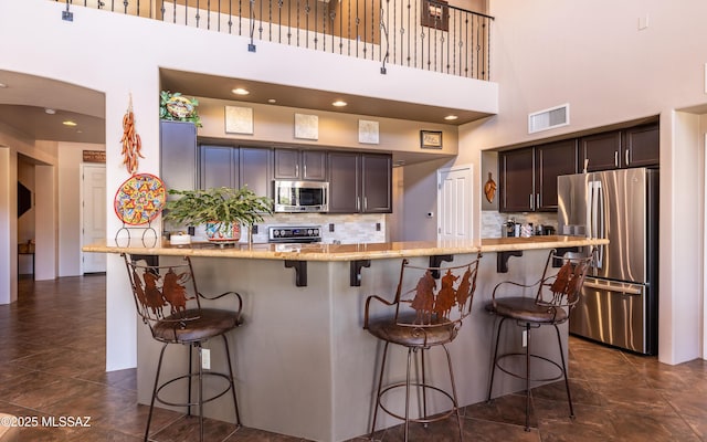 9387 S Via Famero, Vail, AZ 85641 - kitchen with appliances with stainless steel finishes, a high ceiling, dark brown cabinets, light stone countertops, and tasteful backsplash