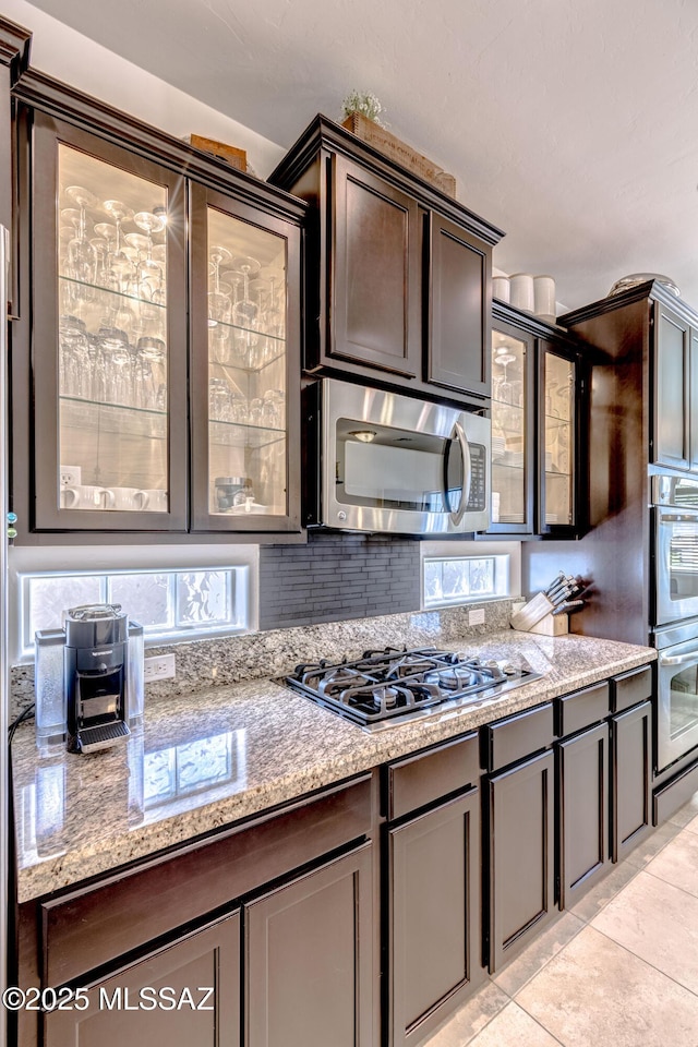 9978 N Niobrara Way, Tucson, AZ 85742 - kitchen featuring appliances with stainless steel finishes, backsplash, glass insert cabinets, dark brown cabinetry, and light tile patterned floors
