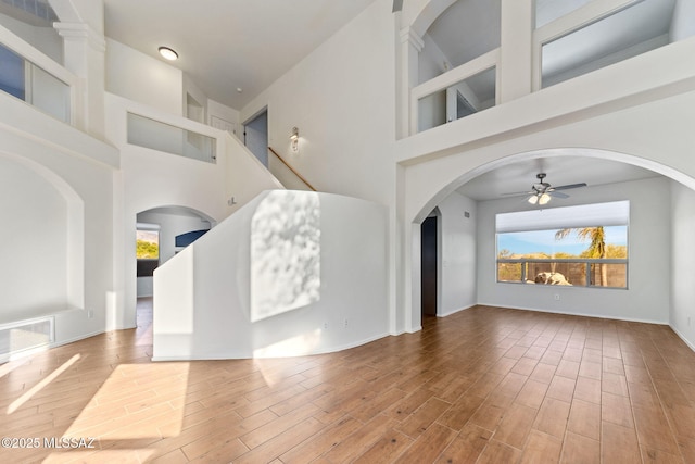 11262 N Chynna Rose Pl, Oro Valley, AZ 85737 - unfurnished living room featuring a towering ceiling, a ceiling fan, wood finished floors, arched walkways, and stairs
