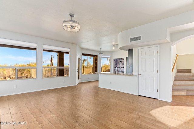 11262 N Chynna Rose Pl, Oro Valley, AZ 85737 - unfurnished living room with light wood-type flooring, a sink, stairs, baseboards, and arched walkways