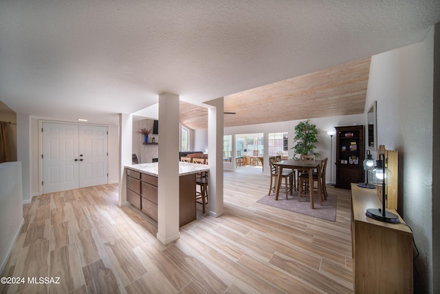 5617 N Camino Del Conde, Tucson, AZ 85718 - kitchen with light wood-style flooring, a kitchen breakfast bar, baseboards, a textured ceiling, and light stone counters