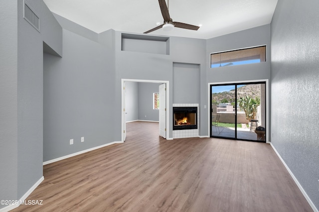 4996 N Valle Rd, Tucson, AZ 85750 - unfurnished living room featuring a towering ceiling, a ceiling fan, wood finished floors, a lit fireplace, and baseboards