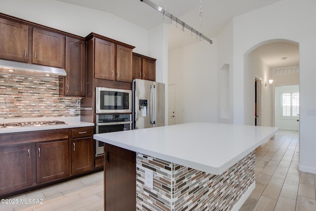 9016 W Birchover Dr, Marana, AZ 85653 - kitchen featuring stainless steel appliances, arched walkways, decorative backsplash, light countertops, and a center island