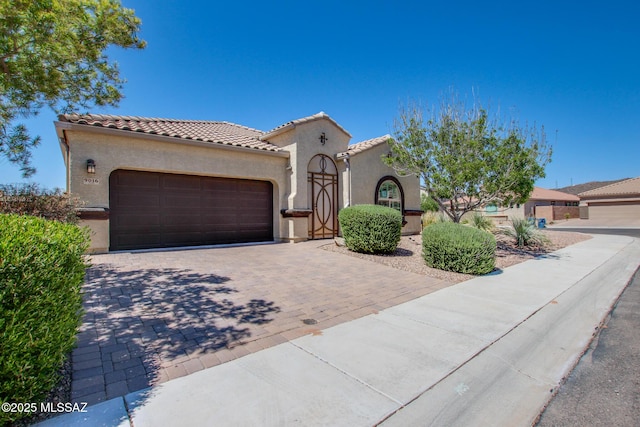9016 W Birchover Dr, Marana, AZ 85653 - mediterranean / spanish-style home featuring an attached garage, stucco siding, decorative driveway, and a tiled roof