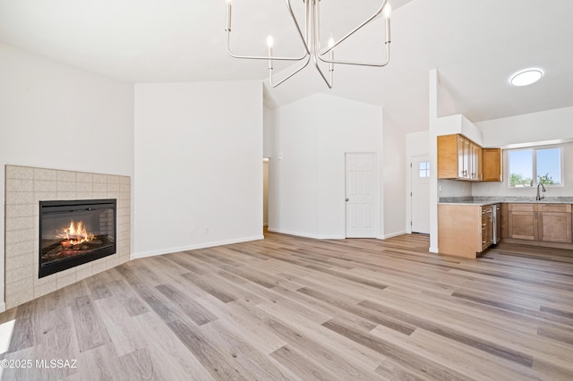 7112 S Haskins Dr, Tucson, AZ 85746 - unfurnished living room with light wood finished floors, vaulted ceiling, a tile fireplace, baseboards, and a chandelier