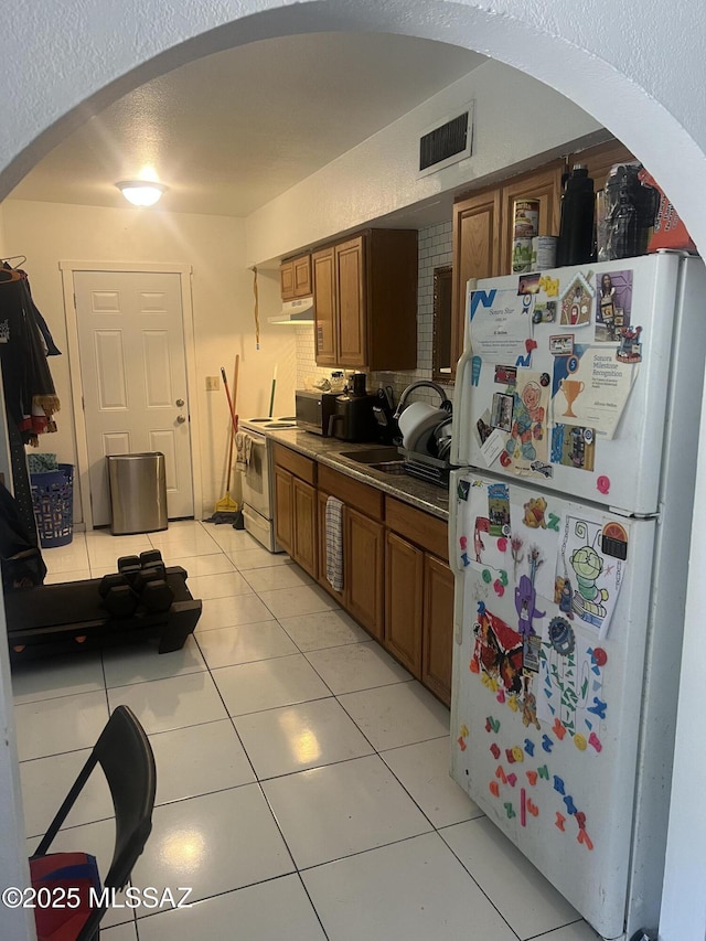 321-323 E Olive St, Tucson, AZ 85706 - kitchen with white appliances, under cabinet range hood, brown cabinets, arched walkways, and light tile patterned flooring