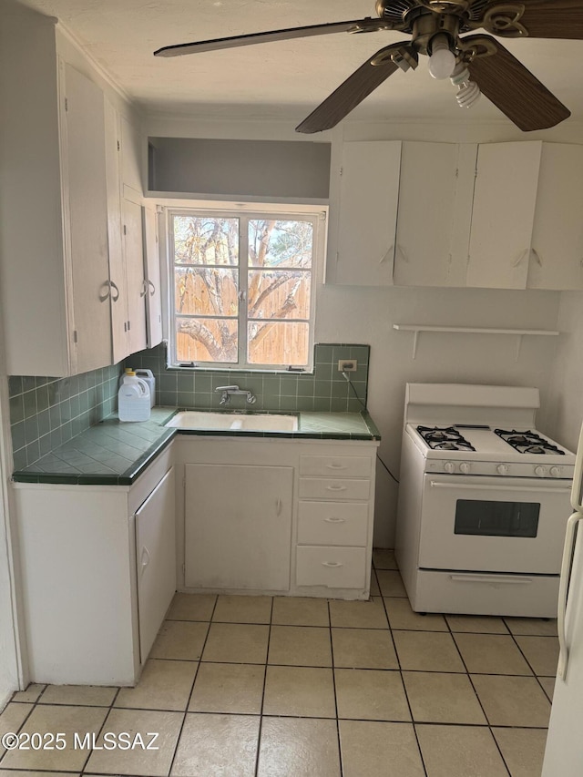 kitchen with white range with gas stovetop, tile counters, white cabinetry, and tasteful backsplash