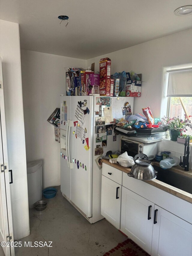 kitchen featuring white cabinets, concrete flooring, and white refrigerator with ice dispenser