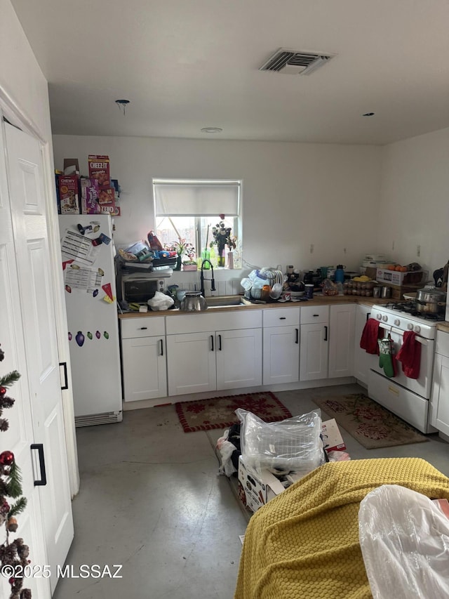 kitchen featuring white appliances, white cabinetry, a sink, and light floors