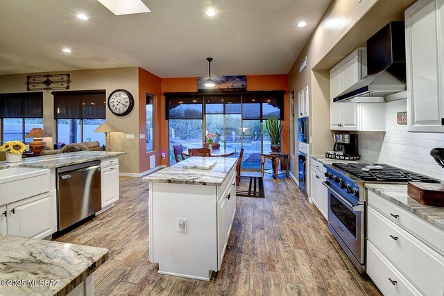 2500 N Fennimore Ave, Tucson, AZ 85749 - kitchen with appliances with stainless steel finishes, wall chimney exhaust hood, a center island, wood finished floors, and light stone countertops