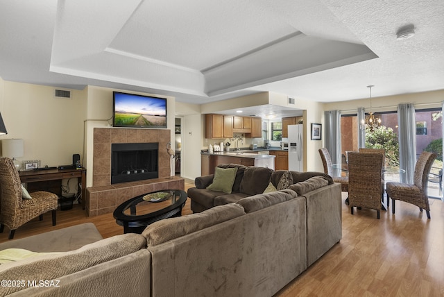 5051 N Sabino Canyon Rd Unit 1107, Tucson, AZ 85750 - living area featuring a raised ceiling, light wood-style floors, a chandelier, and a tile fireplace