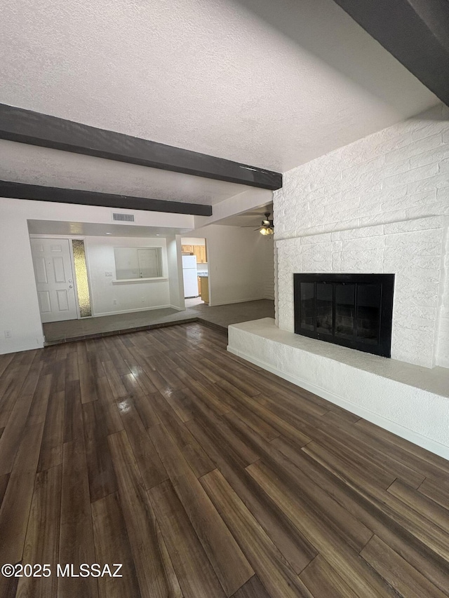 1166 Zircon Ct, Rio Rico, AZ 85648 - unfurnished living room with beam ceiling, wood finished floors, a glass covered fireplace, ceiling fan, and a textured ceiling