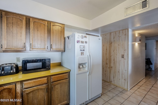 3090 W Alaska St, Tucson, AZ 85746 - kitchen featuring white fridge with ice dispenser, black microwave, light countertops, light tile patterned flooring, and brown cabinets
