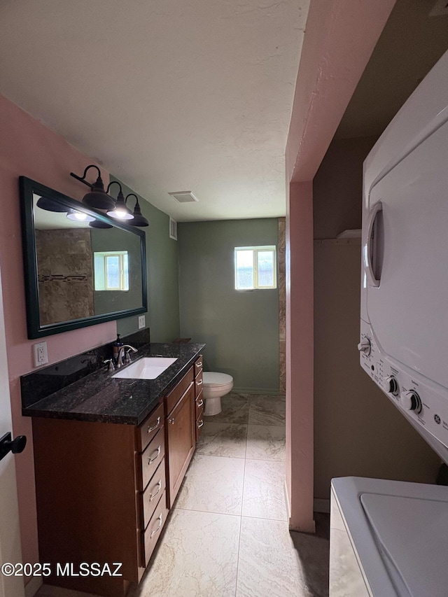140 W 27th St, Tucson, AZ 85713 - bathroom featuring stacked washing machine and dryer, toilet, vanity, and marble finish flooring