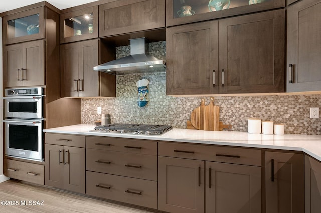 6812 W Cliff Spring Trl, Marana, AZ 85658 - kitchen featuring wall chimney range hood, stainless steel appliances, light countertops, light wood finished floors, and tasteful backsplash