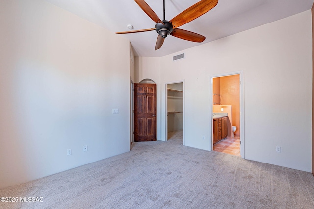 11315 N Mountain Meadow Pl, Oro Valley, AZ 85737 - unfurnished bedroom featuring light carpet, a walk in closet, a closet, connected bathroom, and a ceiling fan