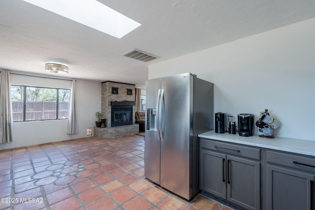 9845 N Volk Ave, Marana, AZ 85653 - kitchen featuring stainless steel fridge, gray cabinetry, light countertops, a brick fireplace, and a skylight