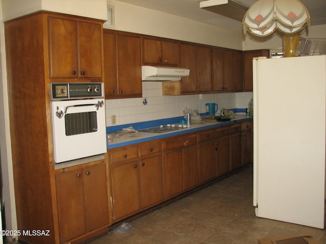 487 E Patrick Dr, Benson, AZ 85602 - kitchen featuring white appliances, under cabinet range hood, decorative backsplash, brown cabinetry, and dark flooring
