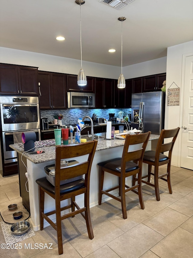 16038 S Camino Casal, Sahuarita, AZ 85629 - kitchen featuring appliances with stainless steel finishes, a sink, decorative backsplash, a breakfast bar, and light tile patterned floors