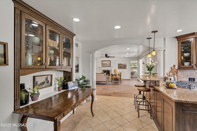 6945 N Mona Lisa Rd, Tucson, AZ 85741 - kitchen featuring arched walkways, a ceiling fan, glass insert cabinets, light stone counters, and light tile patterned floors