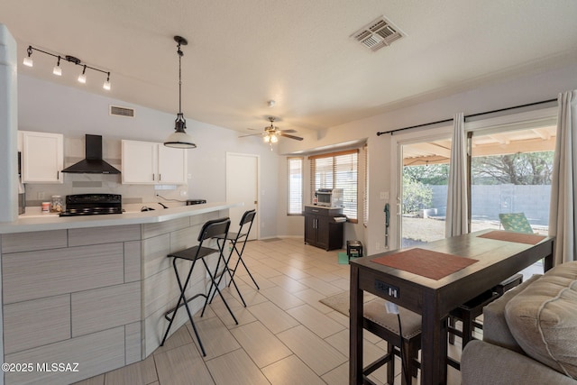 10236 E Rainbow Meadow Dr, Tucson, AZ 85747 - kitchen with wall chimney range hood, black / electric stove, a kitchen bar, a ceiling fan, and light countertops