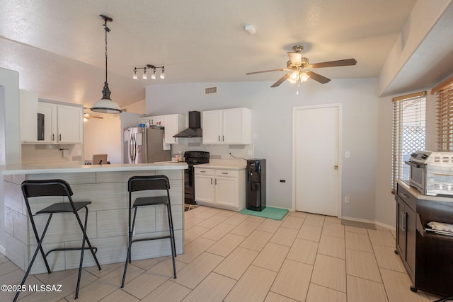 10236 E Rainbow Meadow Dr, Tucson, AZ 85747 - kitchen with freestanding refrigerator, wall chimney range hood, black electric range, a breakfast bar area, and ceiling fan