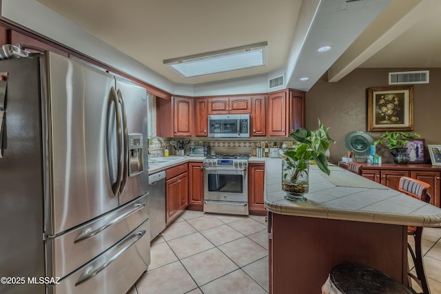 5457 S 13th Ave, Tucson, AZ 85706 - kitchen with stainless steel appliances, tile countertops, a sink, a breakfast bar, and decorative backsplash