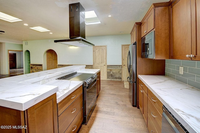 8932 N Rasmussen Ave, Tucson, AZ 85742 - kitchen with island exhaust hood, appliances with stainless steel finishes, brown cabinetry, light wood-style floors, and light stone countertops