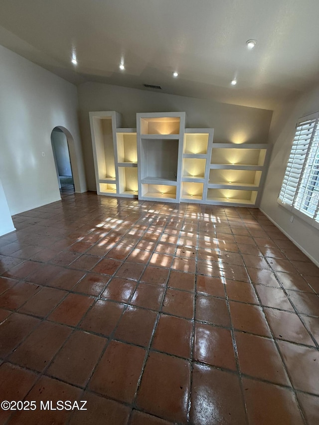 5640 N Placita Favorita, Tucson, AZ 85750 - unfurnished living room featuring arched walkways, dark tile patterned flooring, vaulted ceiling, recessed lighting, and built in shelves