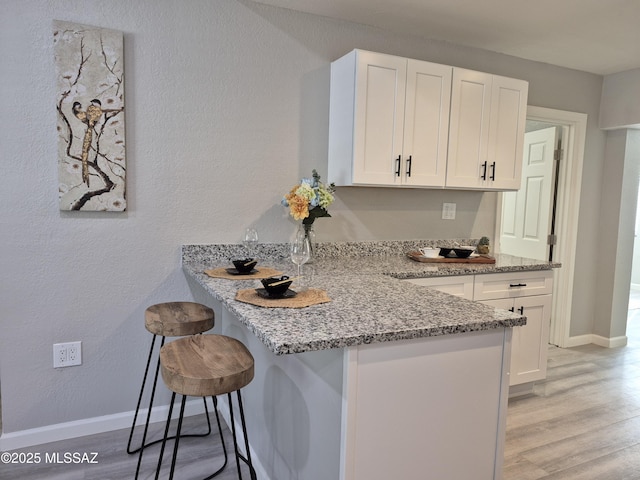 230 N Biddle Ave, Willcox, AZ 85643 - kitchen with white cabinets, a kitchen bar, light stone countertops, light wood-style flooring, and a peninsula
