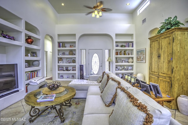 2460 N Cavalry Trl, Tucson, AZ 85749 - living area featuring built in shelves, a towering ceiling, arched walkways, light tile patterned floors, and a ceiling fan