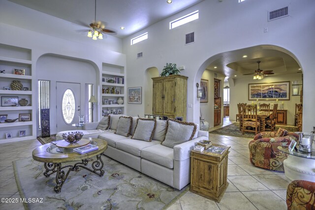 2460 N Cavalry Trl, Tucson, AZ 85749 - living area featuring a ceiling fan, built in features, arched walkways, a high ceiling, and light tile patterned floors