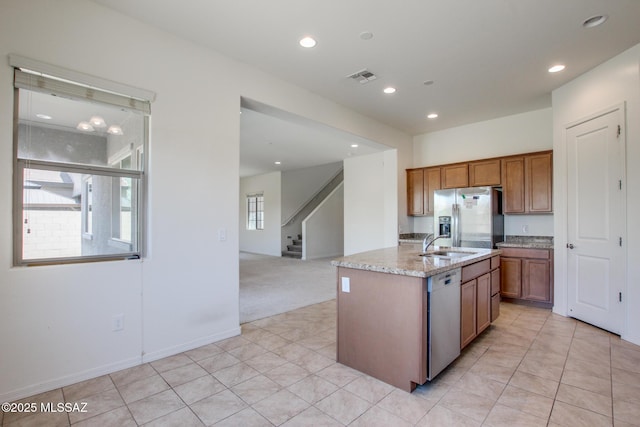 13391 N Flaxleaf Pl, Oro Valley, AZ 85755 - kitchen with stainless steel appliances, brown cabinets, a sink, light stone counters, and a center island with sink