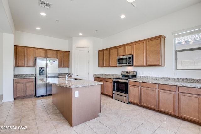 13391 N Flaxleaf Pl, Oro Valley, AZ 85755 - kitchen featuring appliances with stainless steel finishes, a sink, brown cabinetry, light stone counters, and a center island with sink