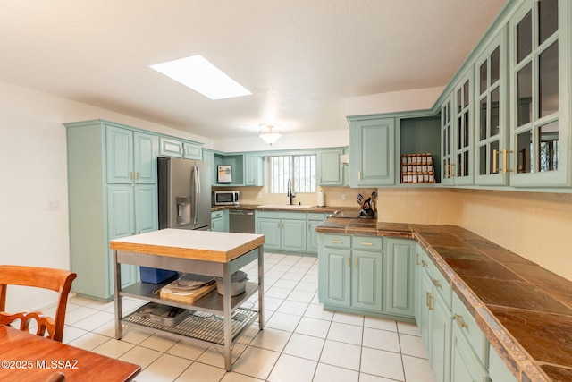 2501 W Calle Paraiso, Tucson, AZ 85745 - kitchen featuring light tile patterned floors, stainless steel appliances, a sink, glass insert cabinets, and a skylight