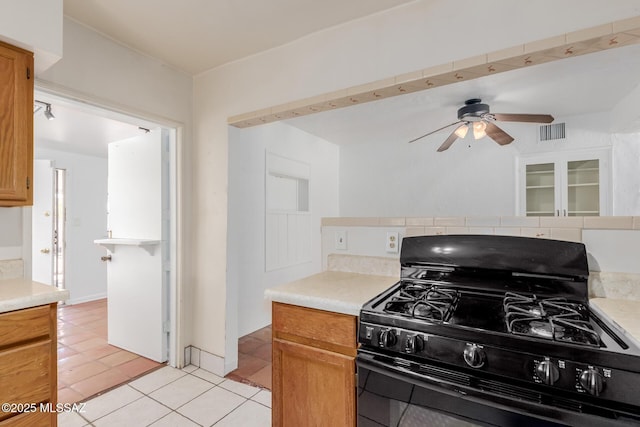1026 E Mitchell St, Tucson, AZ 85719 - kitchen with black range with gas stovetop, light tile patterned flooring, ceiling fan, light countertops, and brown cabinetry