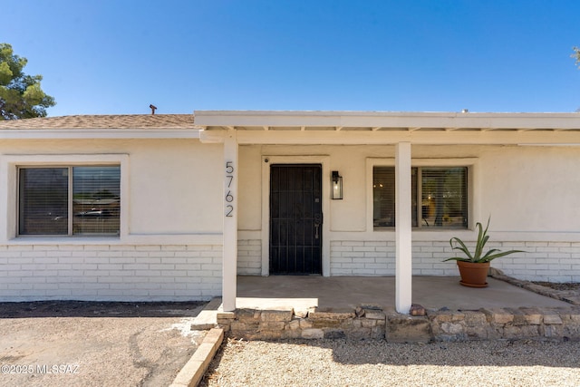 5762 E Helen St, Tucson, AZ 85712 - view of exterior entry featuring brick siding, stucco siding, and roof with shingles