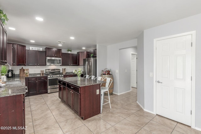 8751 W Saguaro Moon Rd, Marana, AZ 85653 - kitchen featuring appliances with stainless steel finishes, light tile patterned floors, a kitchen breakfast bar, a center island, and dark stone countertops