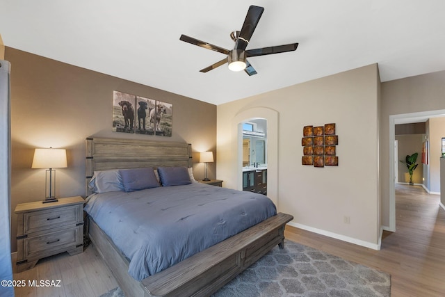 37671 S Hill Side Dr, Tucson, AZ 85739 - bedroom featuring wood finished floors, arched walkways, baseboards, ensuite bathroom, and a ceiling fan
