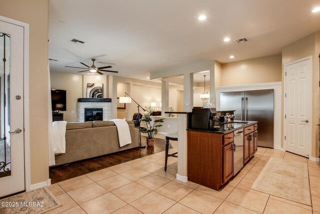 5457 S Canyon Oak Dr, Tucson, AZ 85747 - kitchen with a breakfast bar, stainless steel appliances, a ceiling fan, light tile patterned floors, and a glass covered fireplace