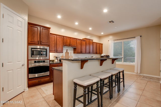 5457 S Canyon Oak Dr, Tucson, AZ 85747 - kitchen with stainless steel appliances, dark countertops, light tile patterned floors, a kitchen breakfast bar, and recessed lighting